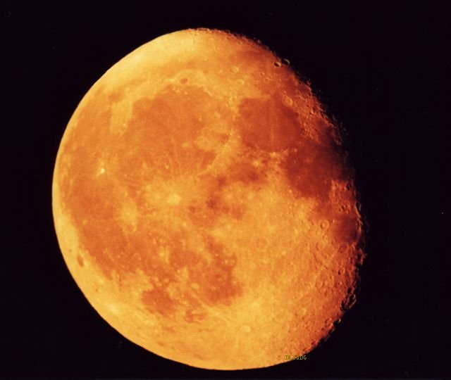 Orange-roter Mond, der gerade aufgegangen ist mit seinen dunklen Flecken und Kratern, die insbesondere zur Seite hin, wo der Mond wegen seiner Phase nicht mehr beleuchtet ist, gut sichtbar sind